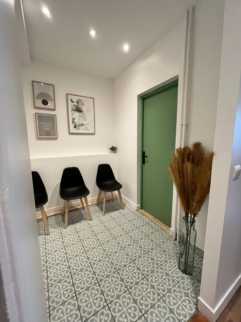 Salle d'attente — 3 fauteuils noirs, carrelage ciment, porte verte, art mural